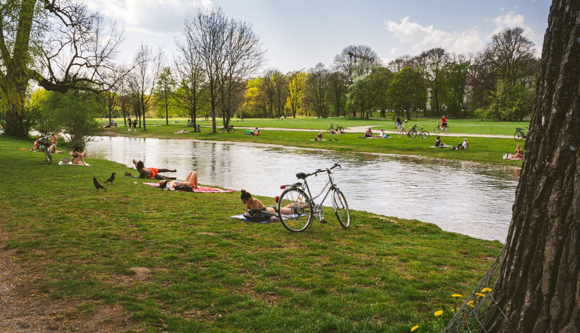 Menschen entspannen auf der Wiese am Wasser im Englischen Garten in München