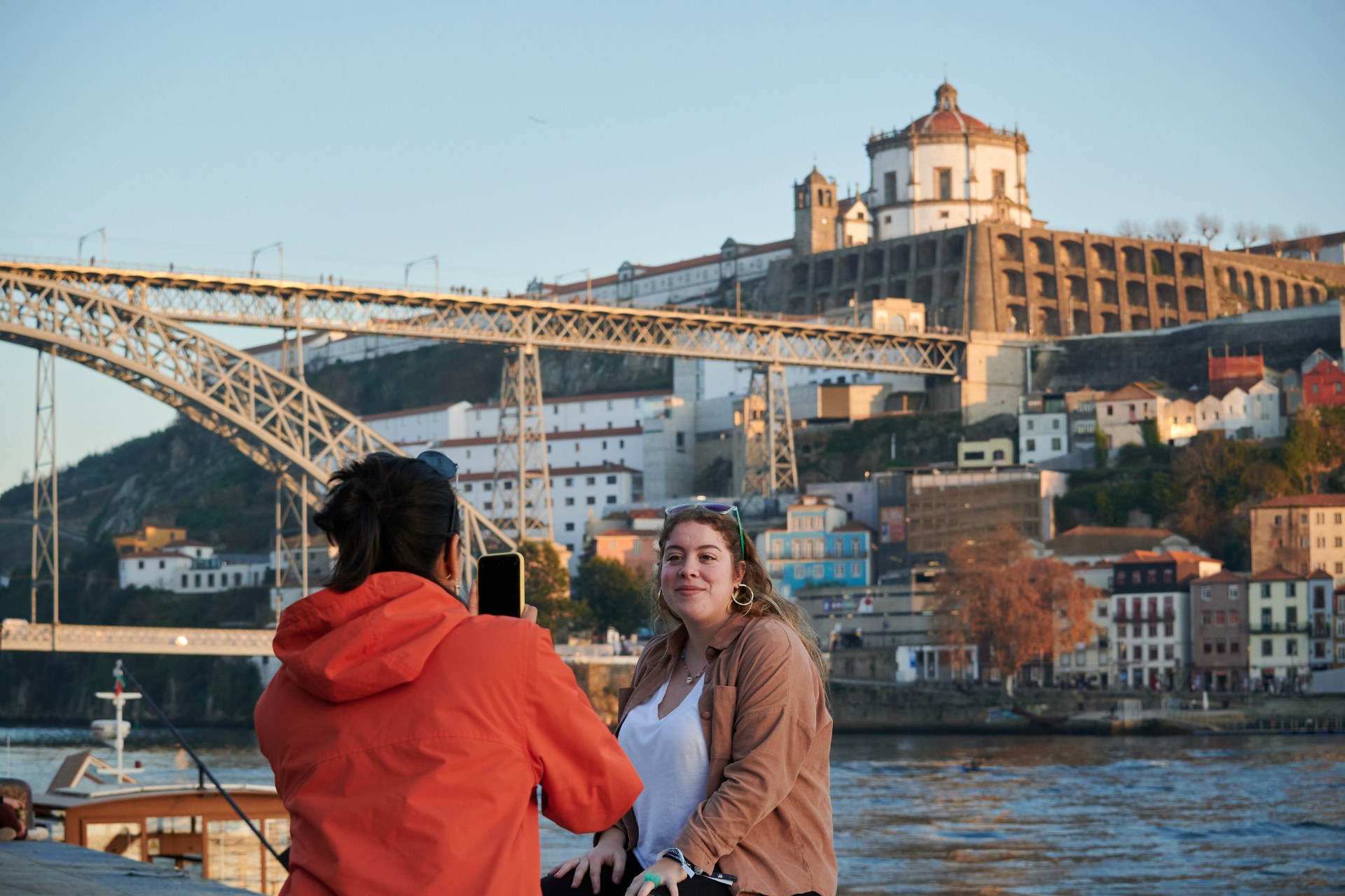 Junge Frau fotografiert ihre Freundin vor einer Brücke in Porto