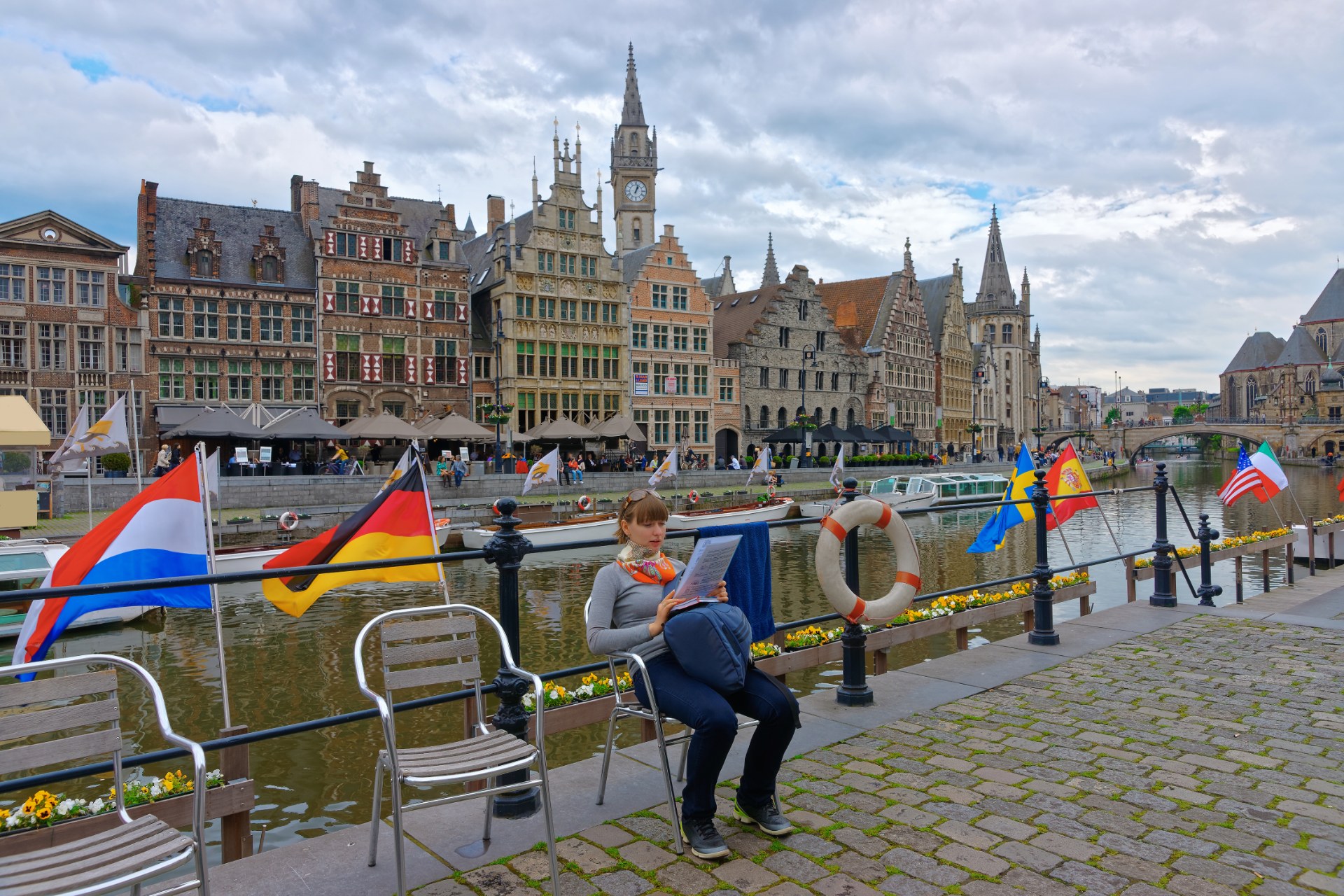 Junge Frau liest am Korenlei-Ufer in Gent, hinter ihr die Häuser der Graslei
