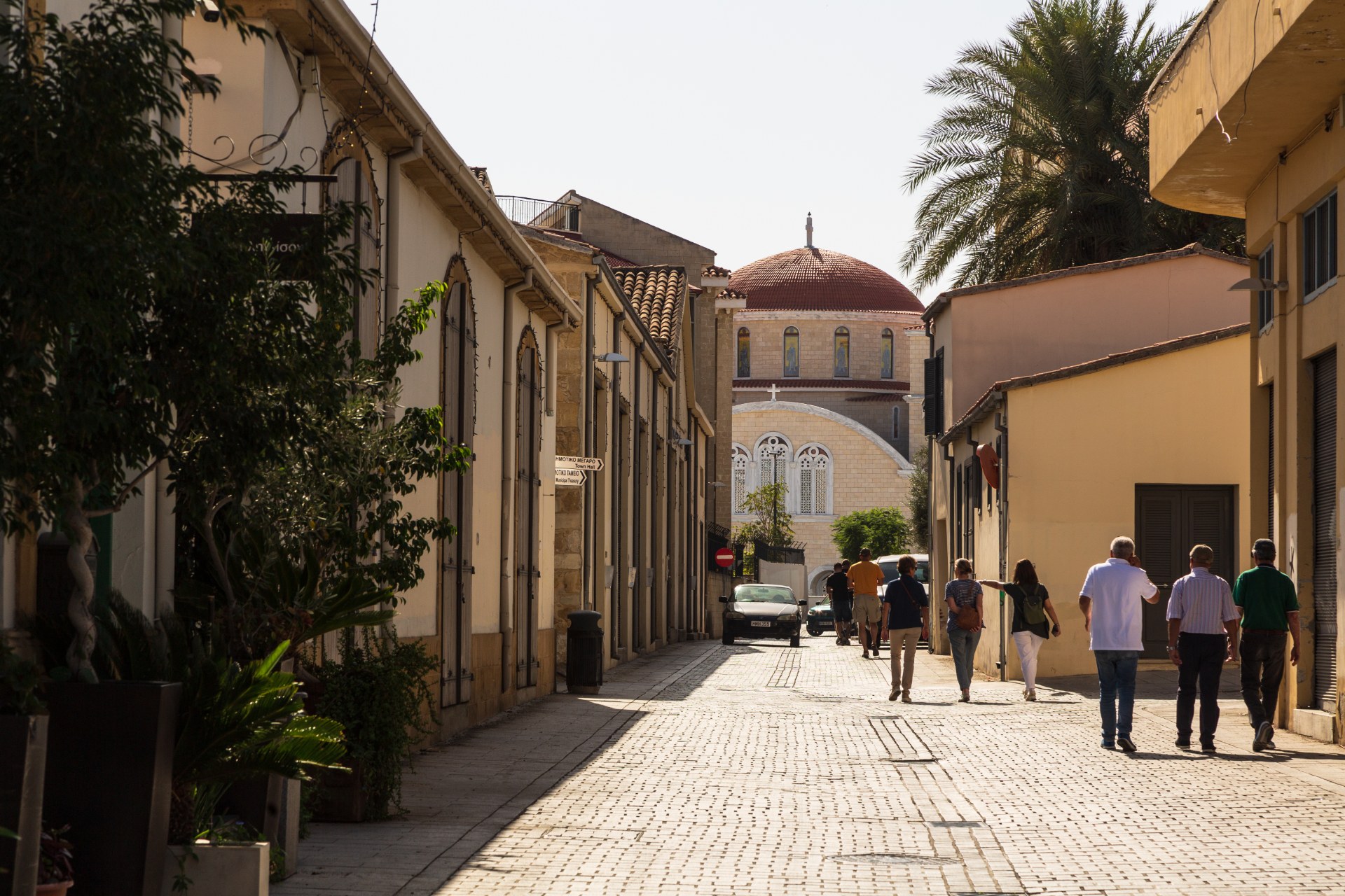 Menschen gehen durch eine enge Altstadtgasse in Nikosia auf eine Kathedrale mit Kuppel zu