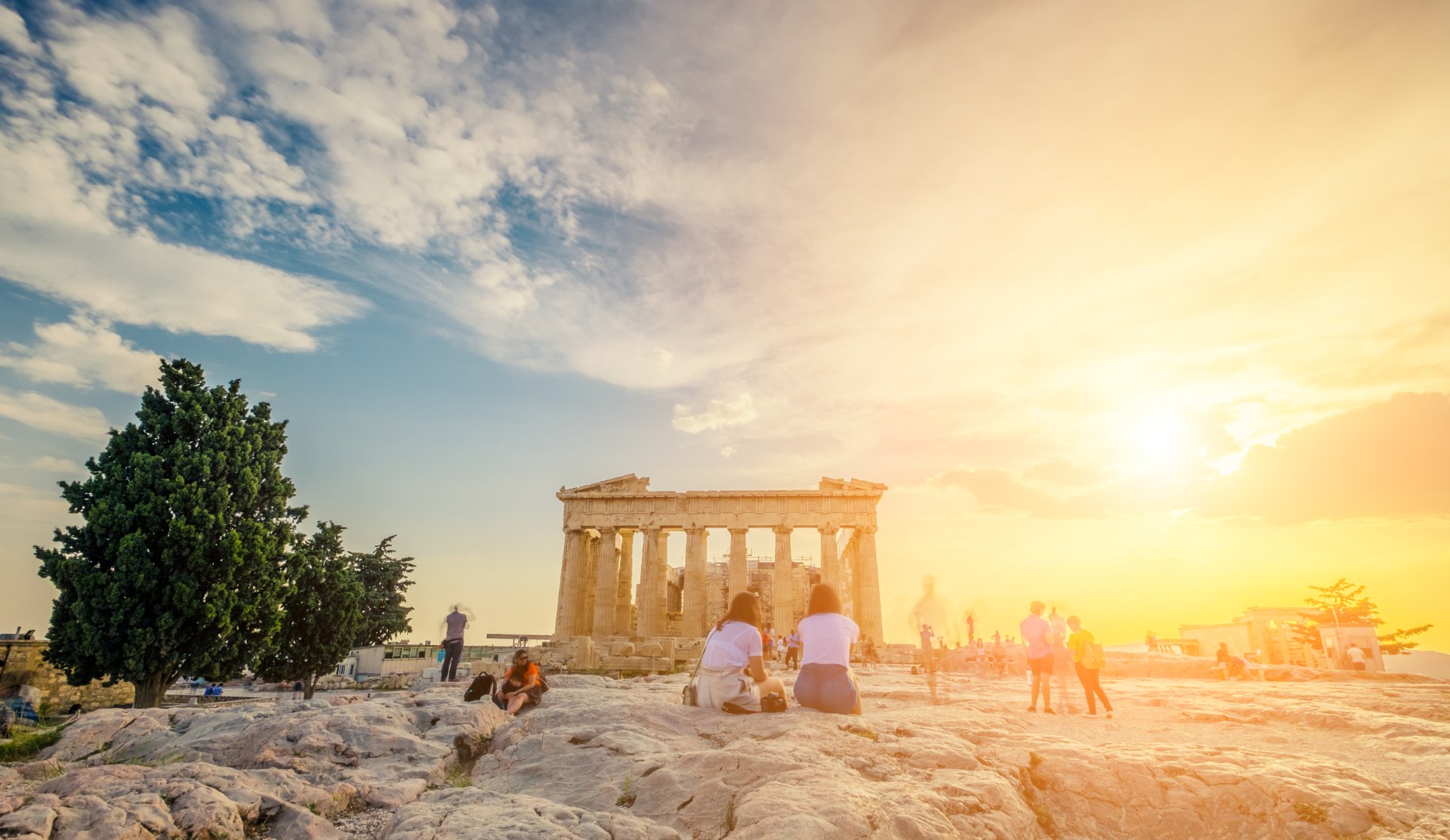 Junge Leute sitzen bei Sonnenuntergang vor dem Parthenon auf der Akropolis