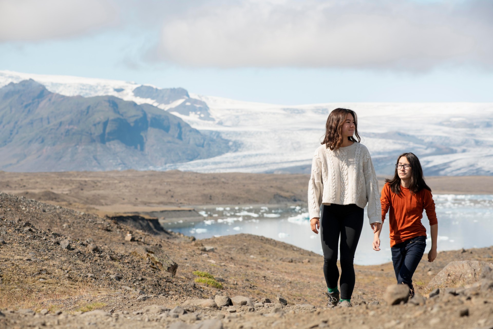 Zwei junge Frauen beim Wandern in Island, hinter ihnen ein Gletscher und Berge